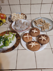 Nabe (hot pot). Shows a kitchen counter with a number of plates ready to be cooked in the hot pot. There's a plate of portobello mushrooms with a flower design carved into the top of them; a bowl of raw shrimp, and a few plates of various vegetables,